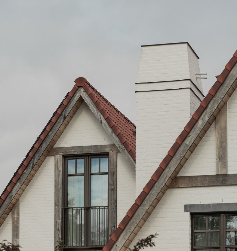 Tuinzicht op een klassieke cottagevilla in Knokke door GC Architecten: witgeschilderde bakstenen gevels met puntgevels, rode pannendaken en witte gemetselde schoorstenen. | © Bert Demasure