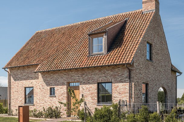 Voorgevel van een landelijke woning met bakstenen muren, houten voordeur en zadeldak