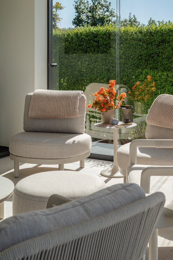 Loungehoek met comfortabele stoelen en bijzettafel in licht poolhouse van GC Architecten