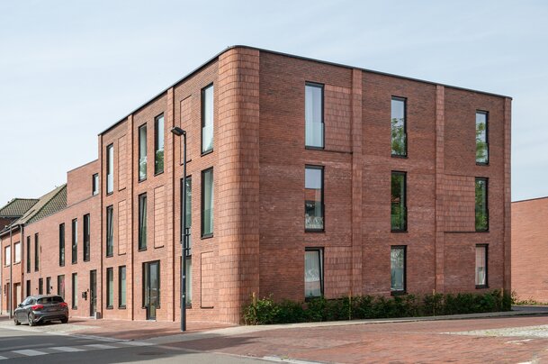 Hedendaags appartementsgebouw van GC Architecten met afgeronde bakstenen hoek en gevarieerde raamritmiek