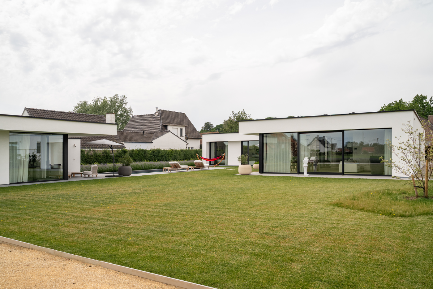 Moderne gelijkvloerse villa met strakke witte gevels, grote glaspartijen en ruime tuin, ontworpen door GC Architecten.