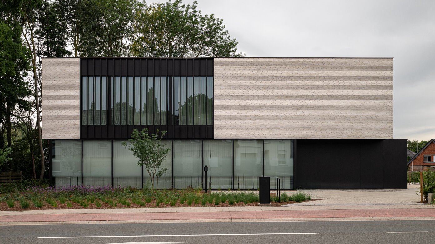 Hedendaags kantoorgebouw met minimalistische architectuur, lichte gevelsteen en grote glaspartijen.