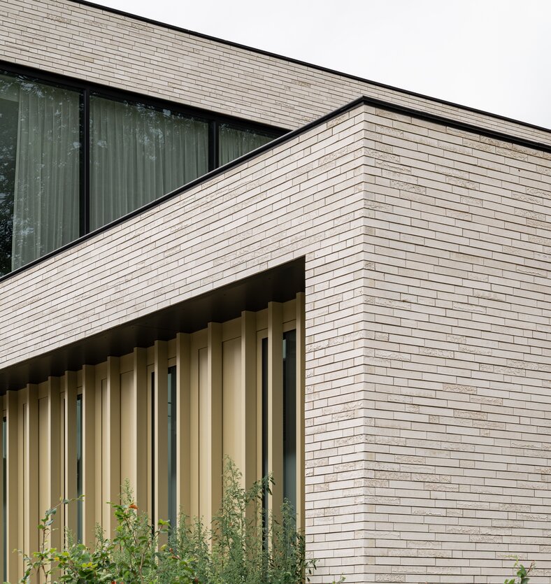 Detail van de moderne kantoorgevel met licht genuanceerde gevelsteen, strakke volumes en verticale aluminium lamellen.