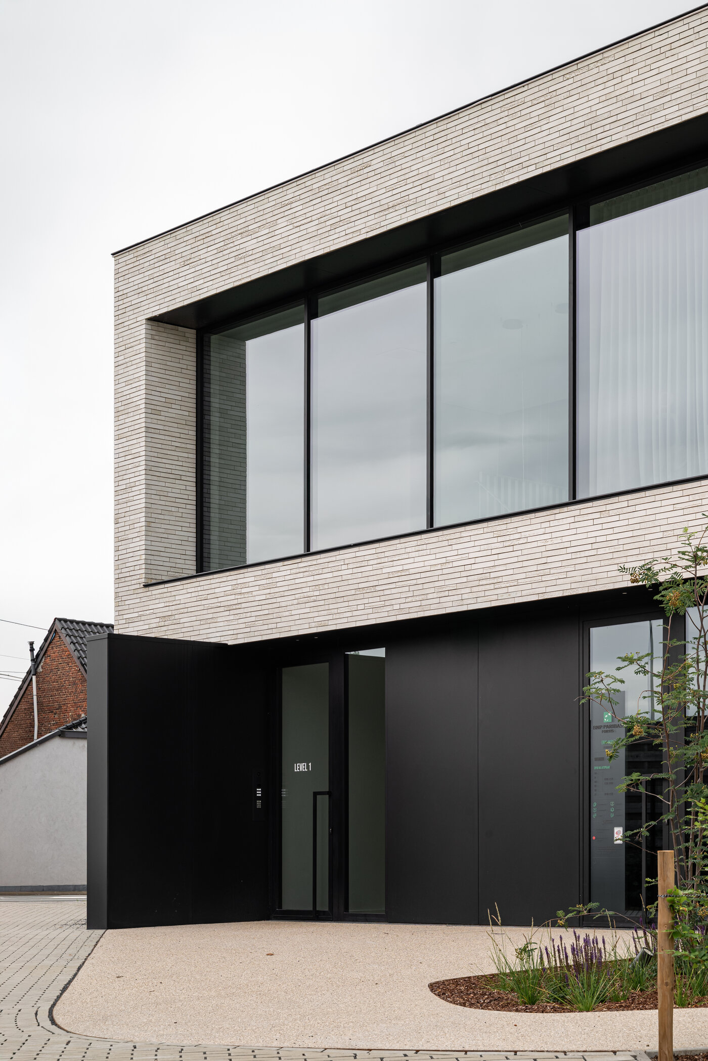Strakke inkomzone van een modern kantoor met zwarte aluminium gevelbekleding en grote glaspartijen.