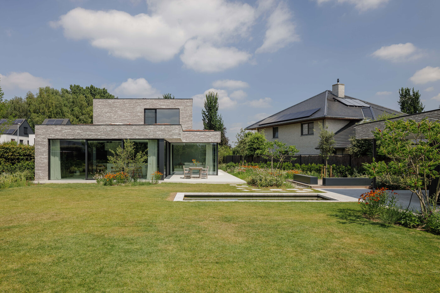Kubistische villa met grote glaspartijen en zicht op eet- en zithoek, met vijver en bloemenweide op de voorgrond, ontworpen door GC architecten.